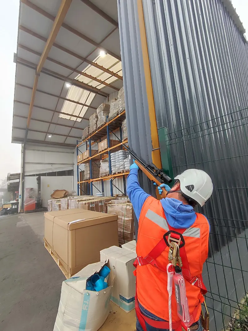 Técnico en altura instalando sistema de exclusión de aves en galpón