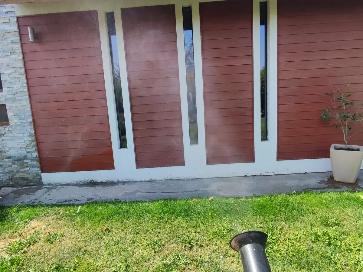 Aplicación con atomizadora motorizada en la fachada y el césped de una casa, vista desde el técnico