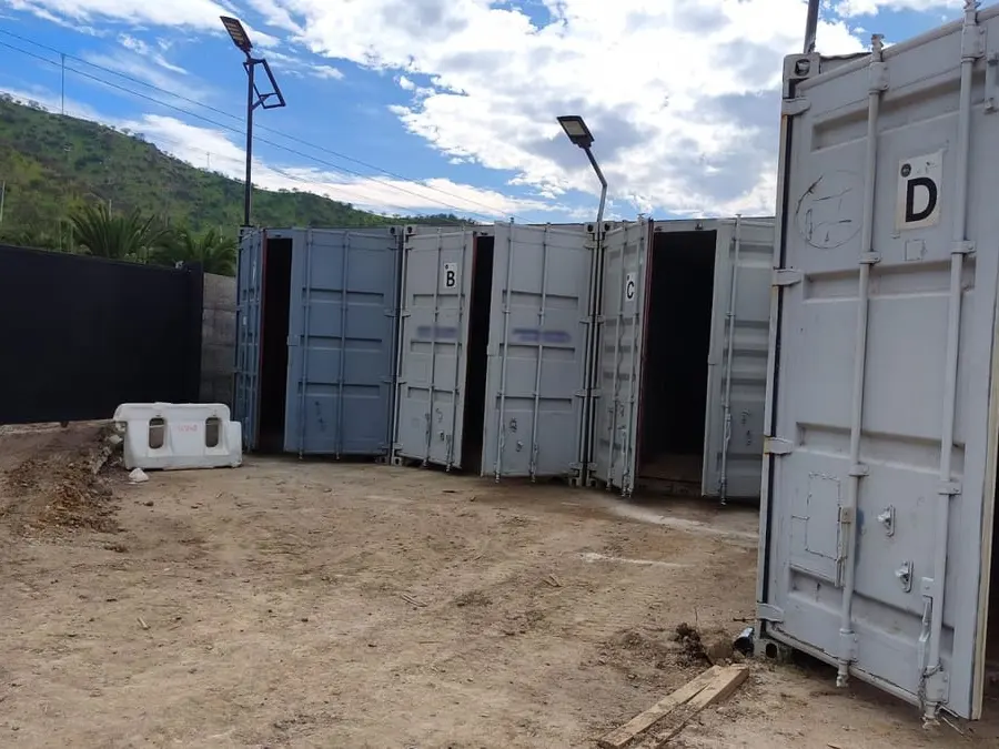 Contenedores metálicos de almacenaje con las puertas abiertas, marcados con las letras B, C y D, en un patio de tierra con cerros al fondo