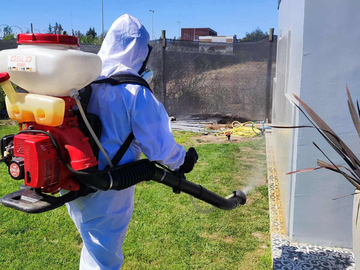 Técnico con traje de protección aplicando con nebulizadora motorizada en el zócalo exterior de una vivienda